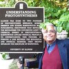 Govindjee stands next to a plaque outside titled "Understanding Photosynthesis."