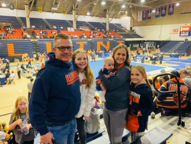 Jennifer Joesting and her family smile in stands at UIUC Women's Gymnastics meet.