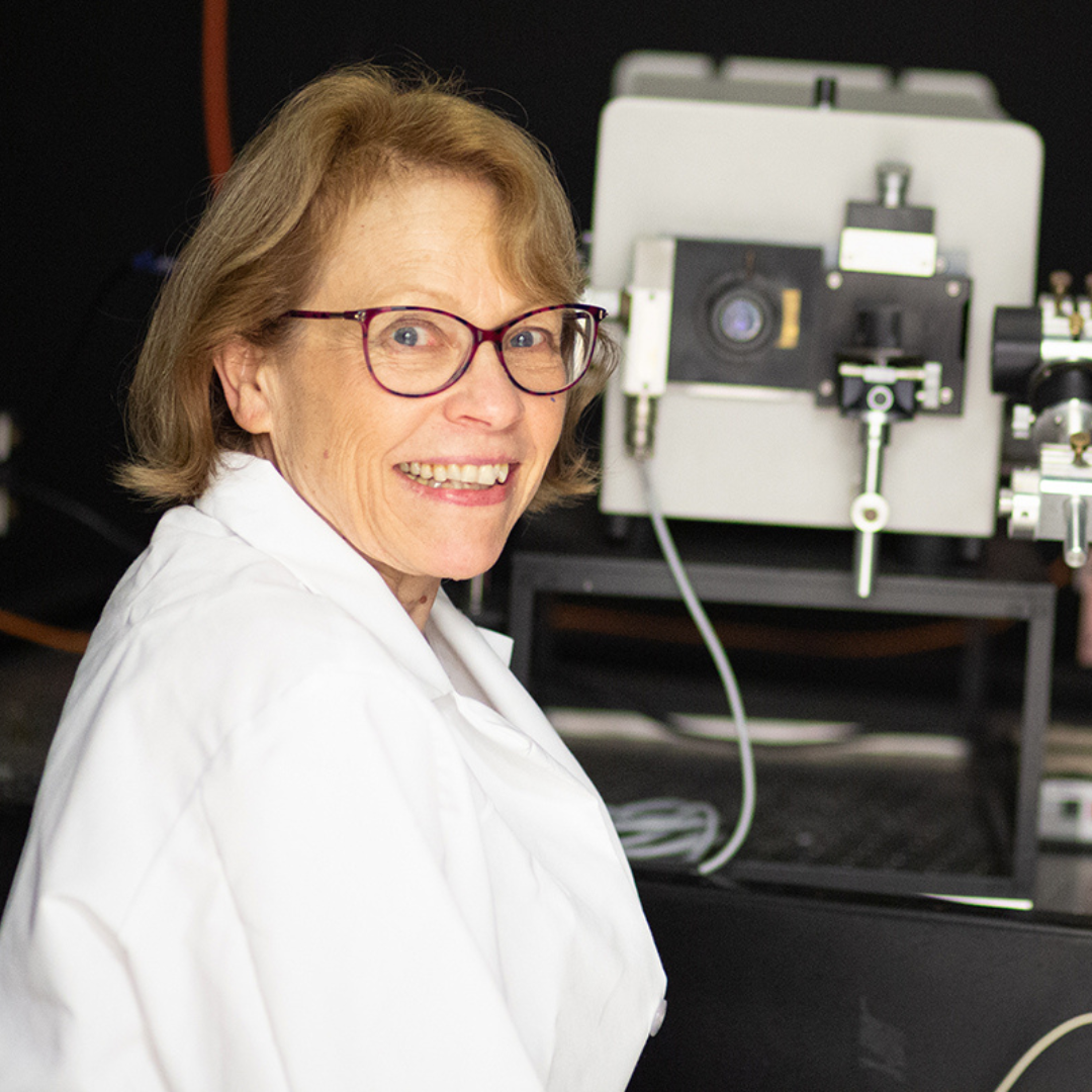 Deborah Leckband smiles for camera while sitting at workspace in lab.