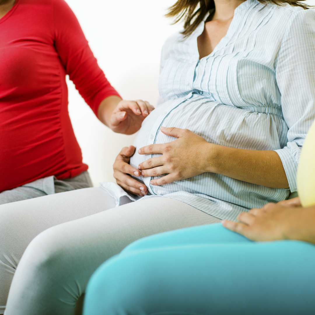 Tight shot of three pregnant women sit side by side, zoomed in on abdominal sections, faces cropped out.