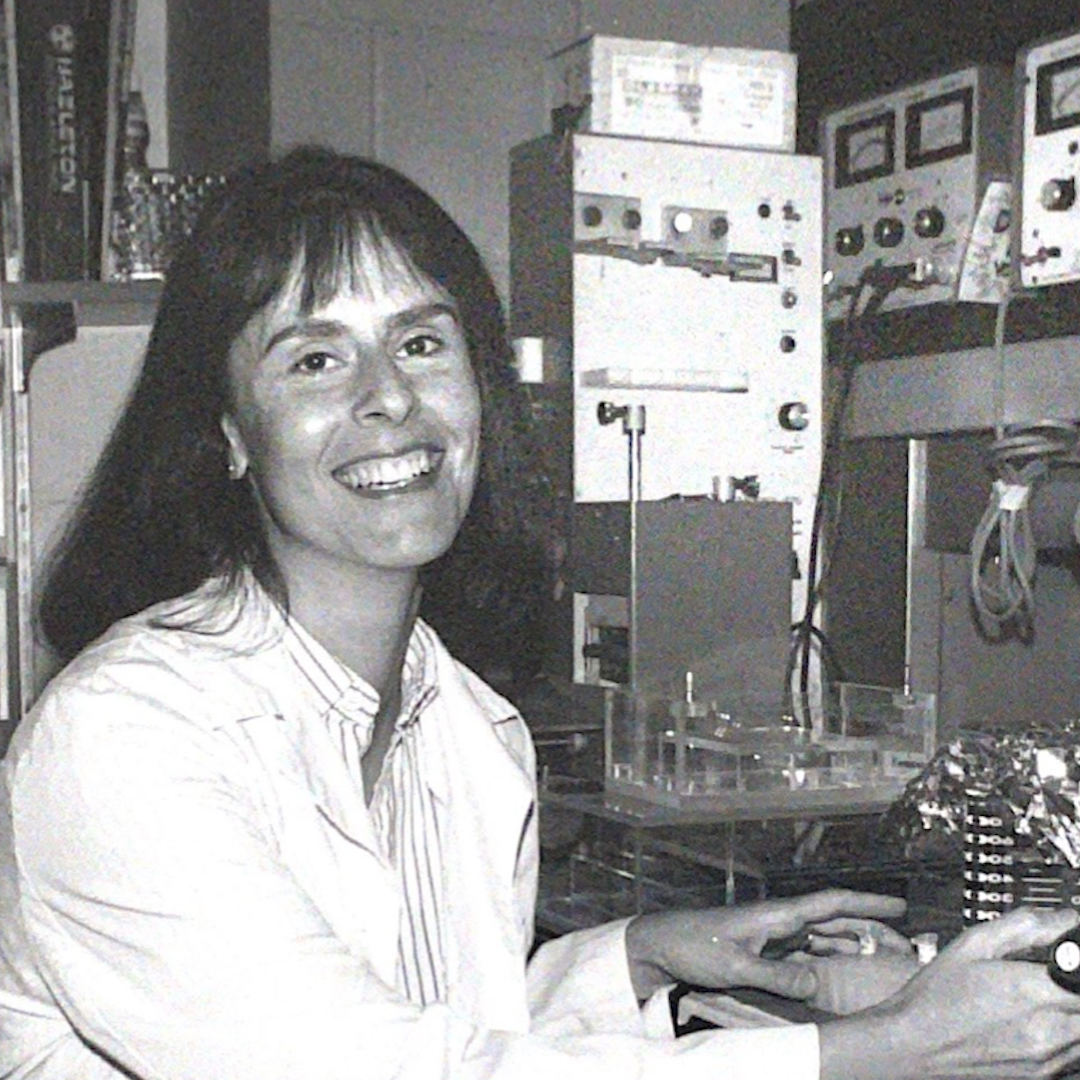 In a black and white photo, Benita S. Katzenellenbogen smiles for camera while sitting in lab.