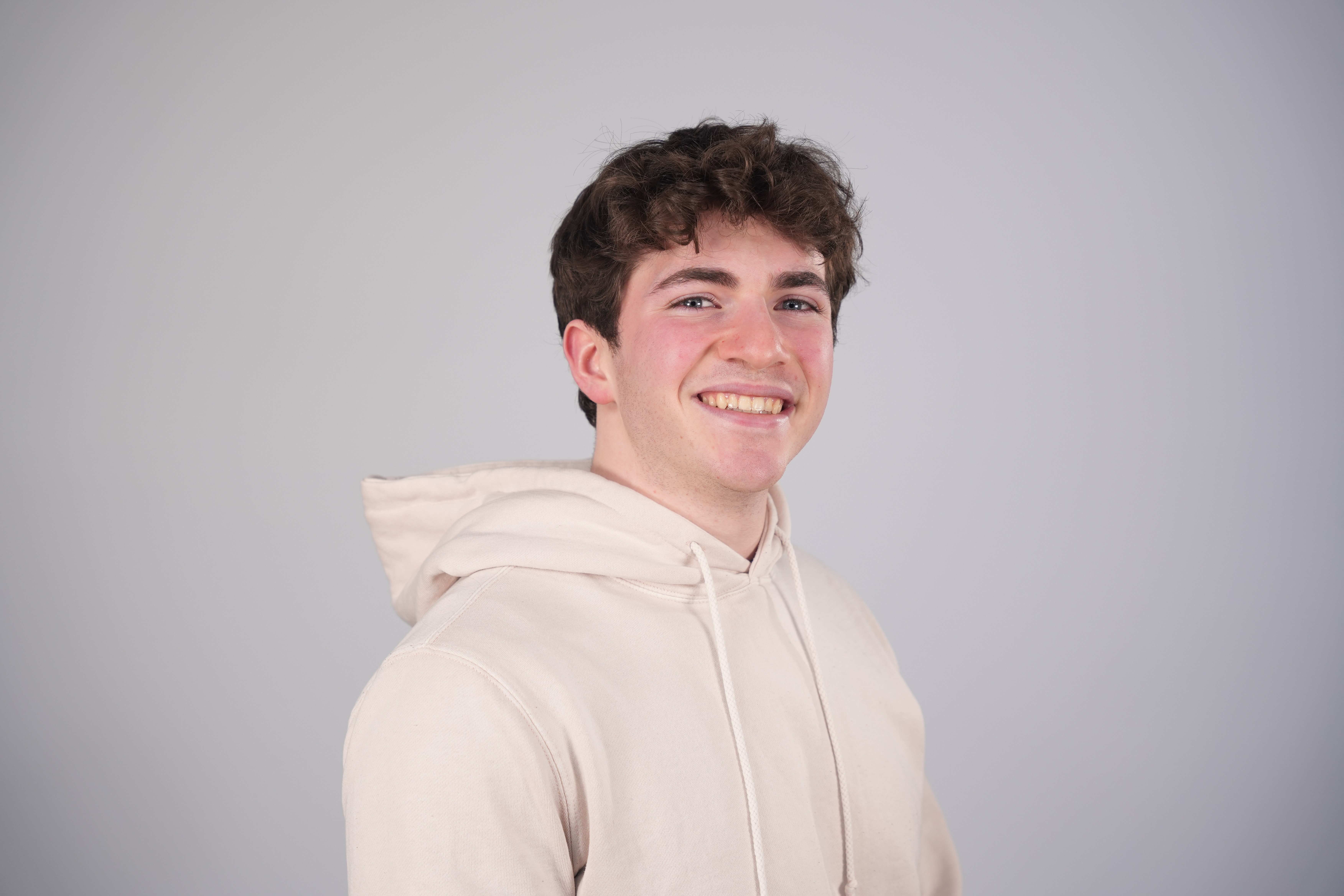 Man in cream hooded sweatshirt poses for headshot in front of grey background