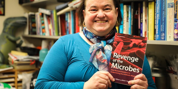 Woman holds book in front of bookshelf