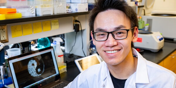 Yiquan Wang smiles while sitting at a desk with an iPad displaying his artwork in the background.