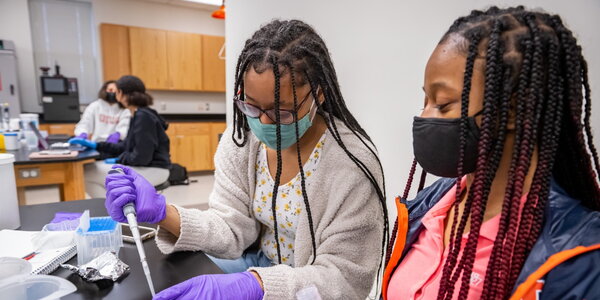 Two students sit together in a lab studying material in a Petri dish. 