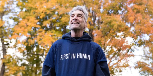 Brian Shelton smiles outside on fall day. Sweatshirt reads First in Human. Credit: Amber Ford for New York Times