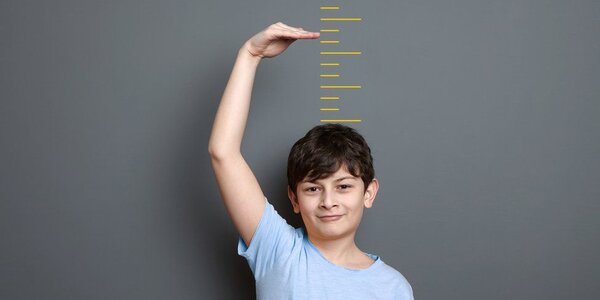 Child stands against wall with measurements, raising his hand several inches above his head. Getty Images