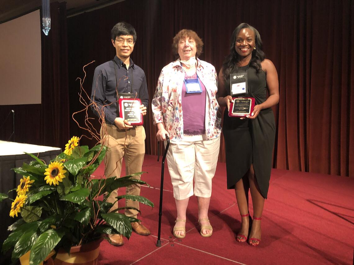 Drs. Nicholas Wu, Ann Palmenberg, and Kizzmekia Corbett stand together for a photo. Wu and Corbett hold up their engraved award plaques. 