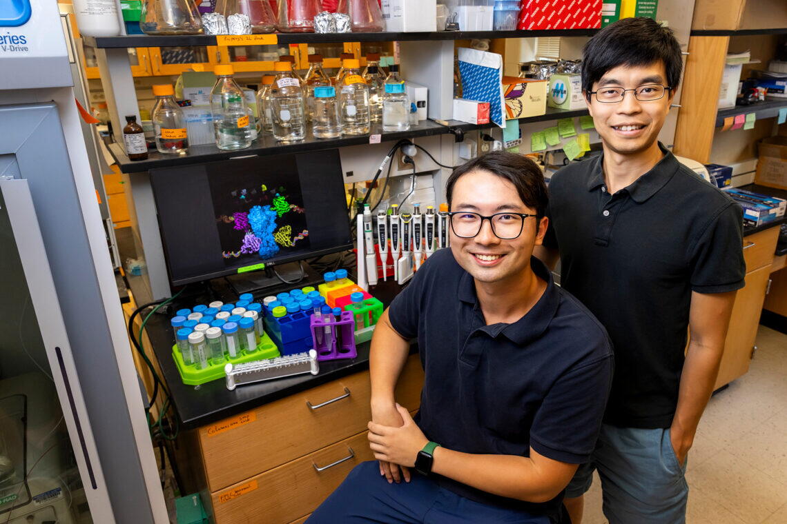 Two men in navy polos stand in front of laboratory bench
