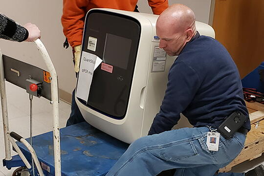 Todd Hawkins, Ironworkers foreperson with Facilities & Services at the University of Illinois, helps to unload a real-time quantitative polymerase chain reaction (qPCR) instrument at Carle Health. The machine has the ability to amplify and identify specific RNA segments within a sample, and is used to assist with COVID-19 testing. (Image courtesy of the Carl R. Woese Institute for Genomic Biology.)