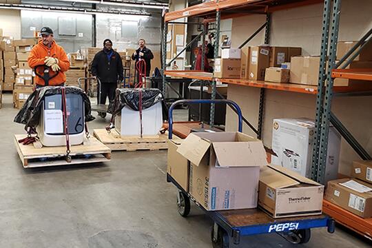 Facilities & Services employees at the University of lllinois prepare to load two real-time quantitative polymerase chain reaction (qPCR) instruments to deliver to Carle Health. The machines have the ability to amplify and identify specific RNA segments within a sample, and is used to assist with COVID-19 testing. (Image courtesy of the Carl R. Woese Institute for Genomic Biology.)