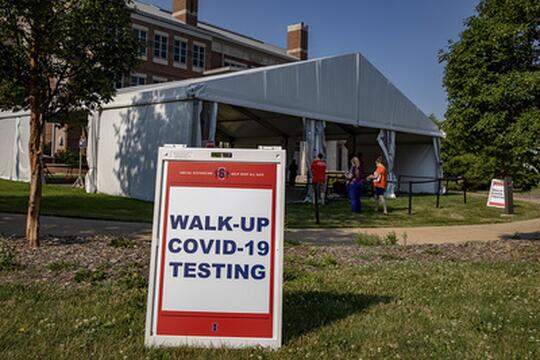 A sign outside a large tent on campus reads "WALK-UP COVID-19 TESTING"