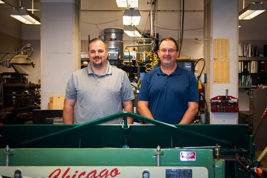 Jared Bear and Scott Baker stand next to each other in the machine shop in Burrill Hall