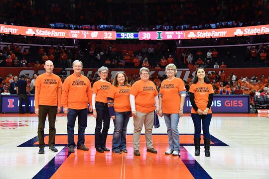 Members of the Cancer Research Advocacy Group stand in the middle of the basketball court of the State Farm Center wearing Krush Cancer orange shirts.