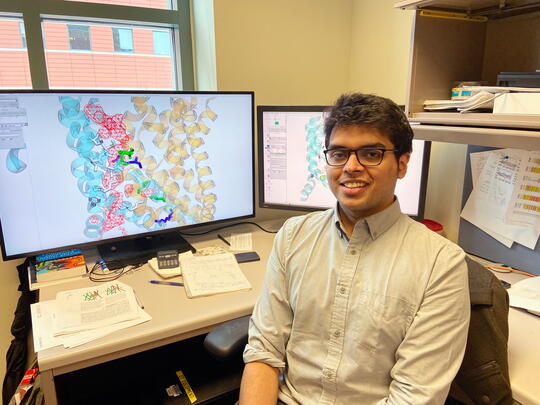 Shashank Pant sits in front of two computer monitors displaying data.