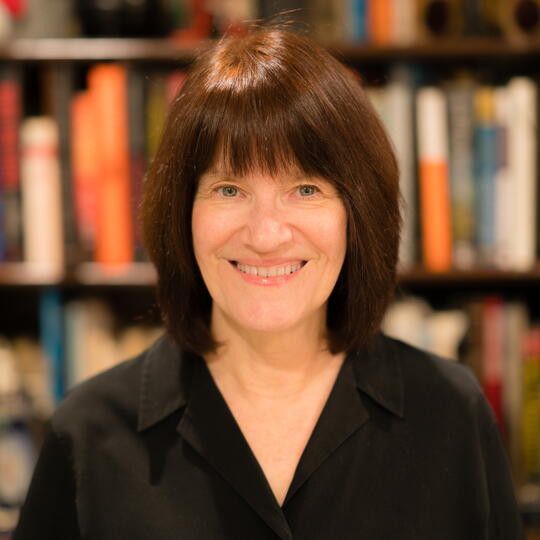 Photo of Carole Stivers smiling, with bookshelves in the background.