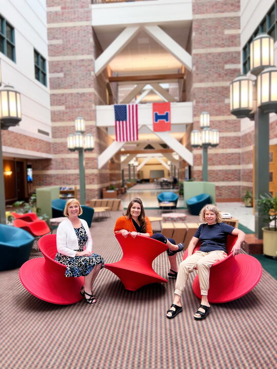 Three women balancing on red swivel chairs.