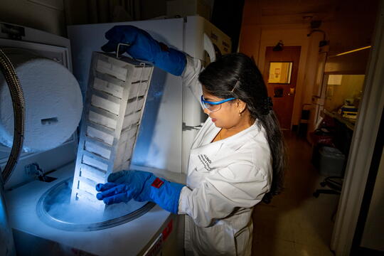 A woman in a white lab coat and protective goggles handles dry ice