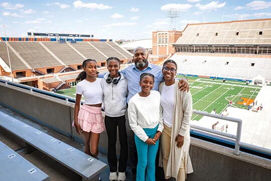 A young family smiles in front a football field.