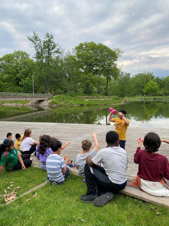 students gather by a pond to watch a science experiment