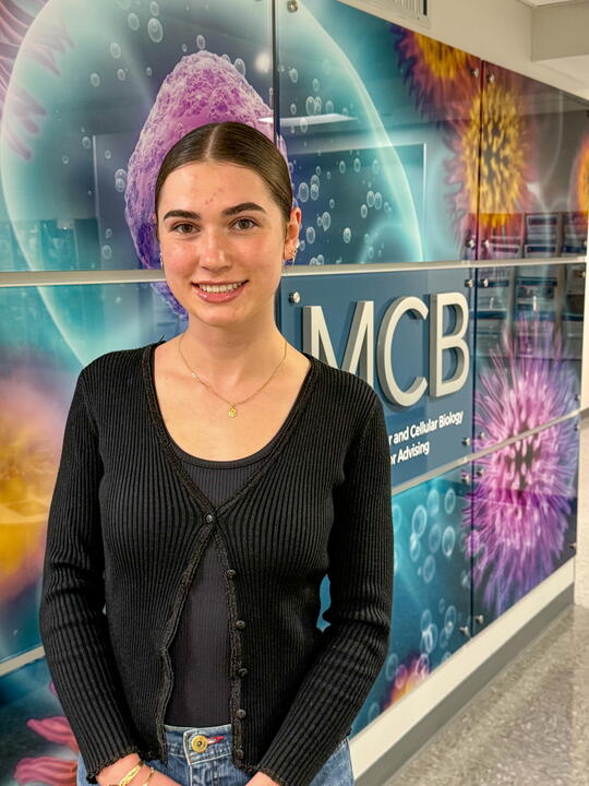 A woman in a black cardigan standing in front of a brightly colored mural.