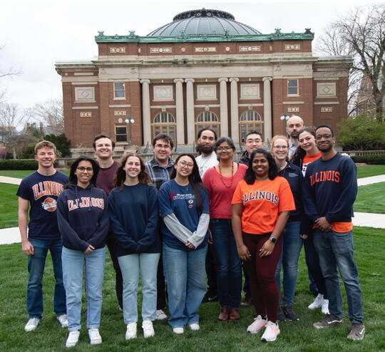 Members of the Anakk lab stand outside on the Quad wearing a variety of orange and blue Illini apparel