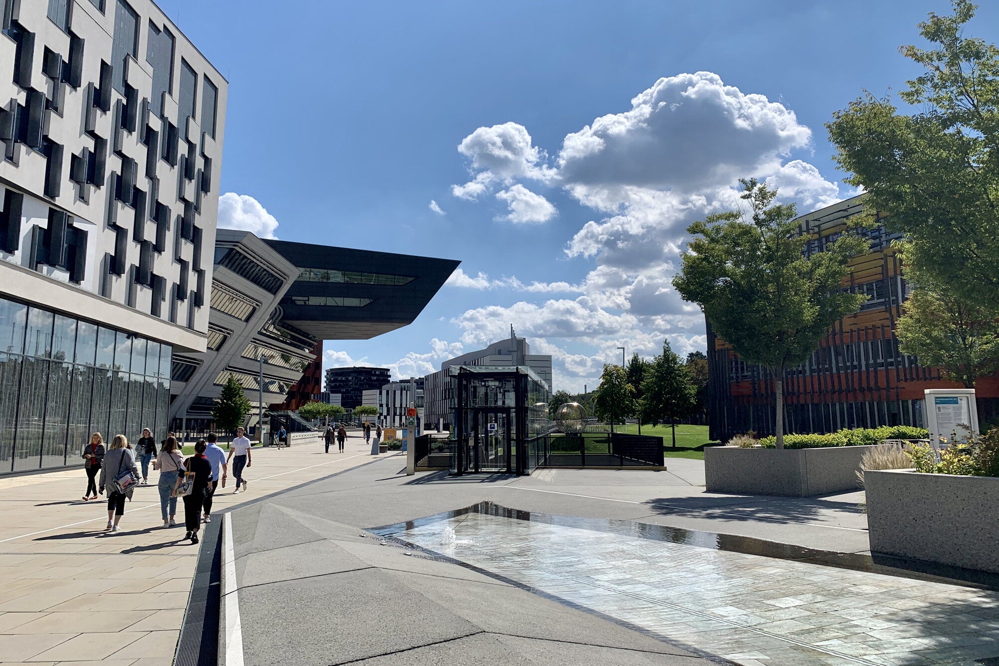 Sunny day on Vienna University campus, next to water fountain and modern university buildings. 
