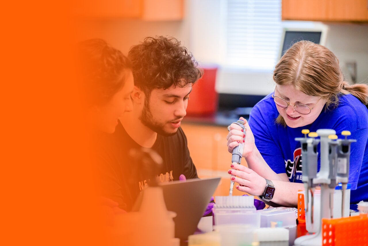 Three students in a lab with an orange gradient background.