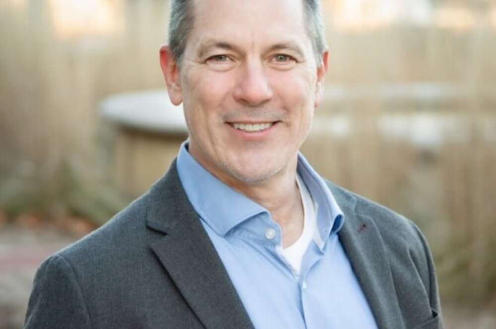 Brian Freeman poses for headshot, smiling, outside.