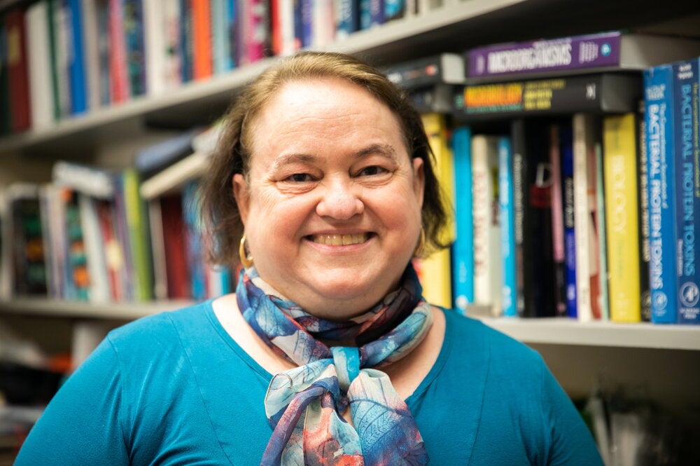 A smiling woman standing in front of a bookshelf wearing a blue shirt and scarf