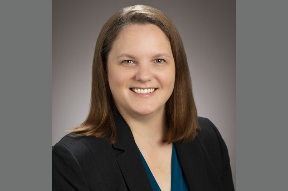 A smiling woman with brown hair wearing a black blazer.