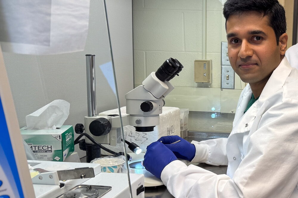 man in labcoat sits in front of a microscope
