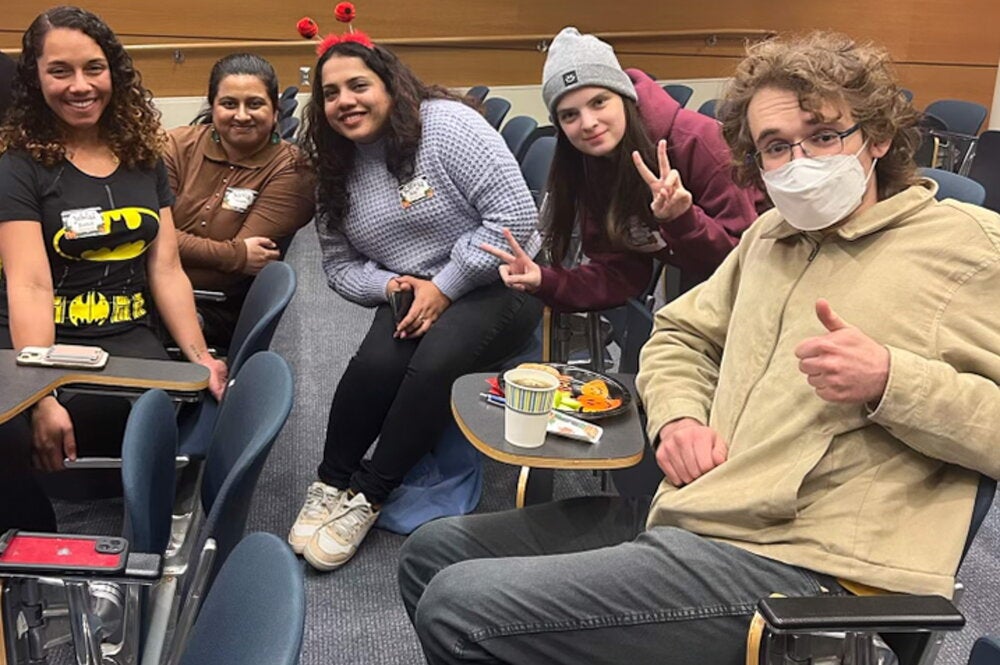 graduate students and their peer mentors give thumbs up and peace signs to camera while sitting in an auditorium