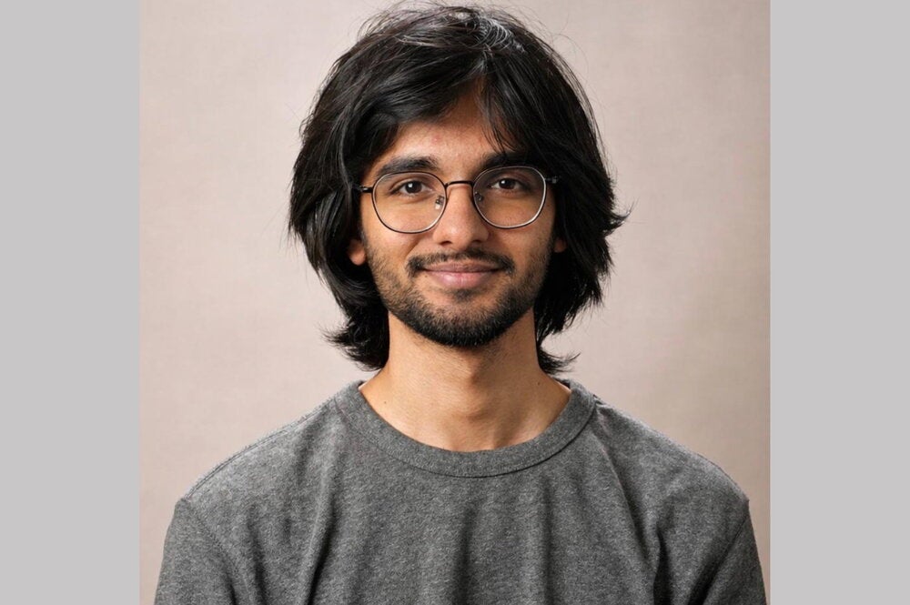 Man with black hair and glasses and beard wearing grey T-shirt