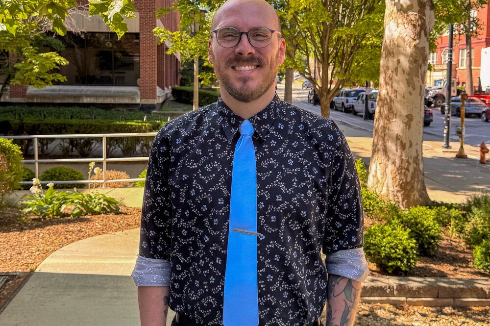 Man with glasses and short beard stands in front of tree outside Burrill Hall