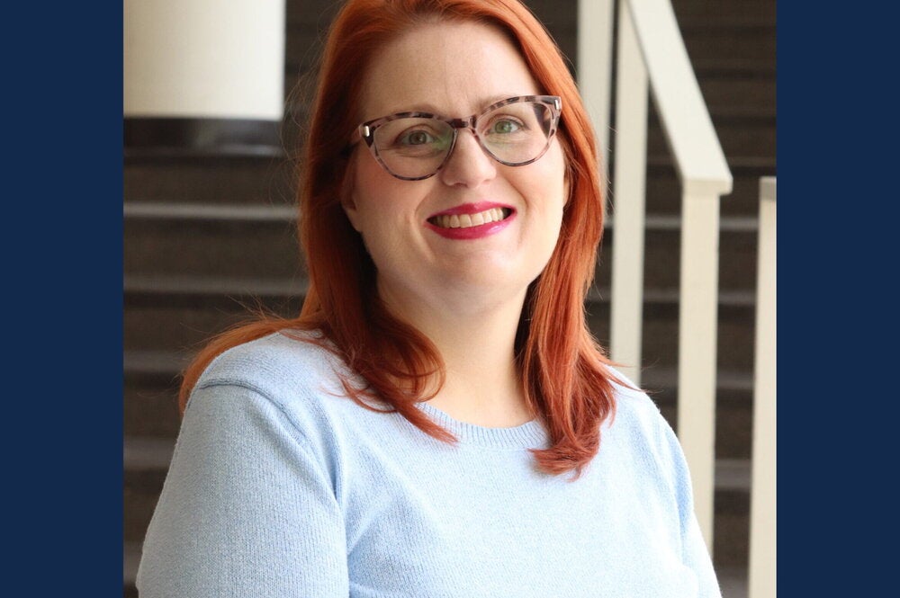 Woman with shoulder length red hair and eyeglasses wears light blue sweater