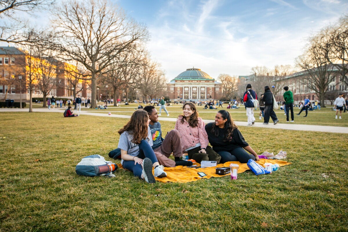 Four students siting on a blanket on the Quad.