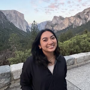 Angela Cabrera smiles for the camera outside with mountains and forest trees in the background.