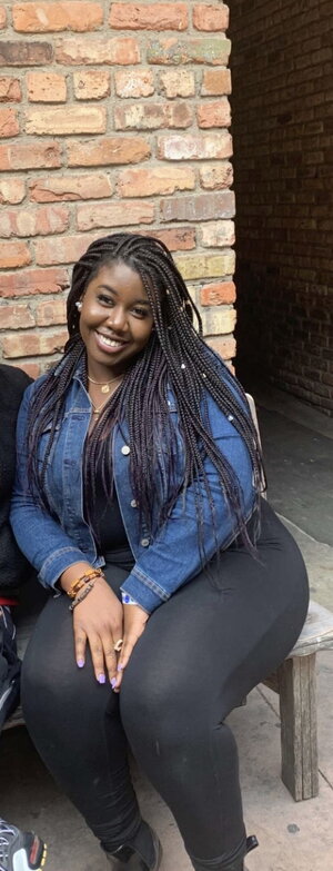 Zainap Umardeen sits smiling outside with a brick wall in the background.