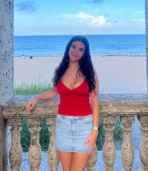 woman in red shirts stands on balcony overlooking a beach