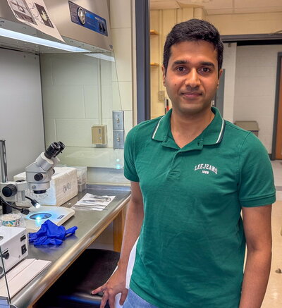 Man in green shirt stands by microscope