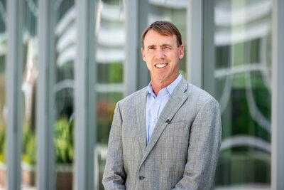 Man in grey suit stands outside modern building