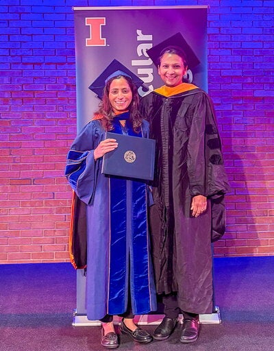 PhD graduate and her advisor stand on a stage at Krannert Center