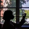 Silhouette of Preeti Sharma holding up a 250 ml pyrex vial with a bit of liquid inside against a window.