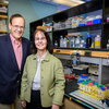 John Katzenellenbogen, left, Benita Katzenellenbogen, right, stand together in front of a lab bench, smiling for the camera. 