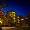 Exterior of Beckman Institute at nighttime. Lights in the building are on and trees along path to the building are illuminated.