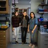 Three scientists in the Mera Lab, Stephanie Puentes-Rodriguez, Paola Mera, and Inoka Menikpurage, stand together smiling for the camera. They are in the doorway leading from one lab space to additional lab space. They are all smiling.