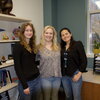 Three women smile while standing in front of a bookcase.