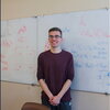 A man in a red shirt and glasses standing in front of a whiteboard.