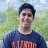 A man in a blue and orange shirt standing in front of a tree line.